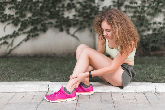 Young athlete sitting outdoors holding her ankle showing foot pain after exercise