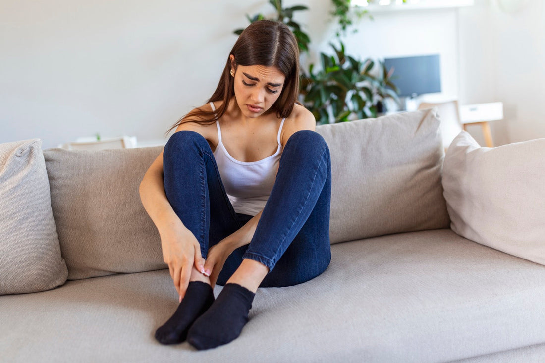 Woman sitting on sofa at home holding her sore foot showing signs of plantar fasciitis
