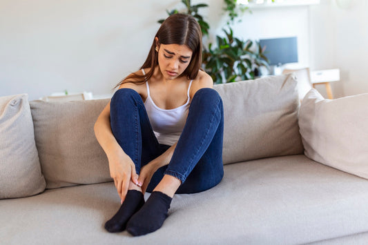 Woman sitting on sofa at home holding her sore foot showing signs of plantar fasciitis