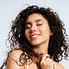 Woman with curly hair smiling against a light grey background - customer review image